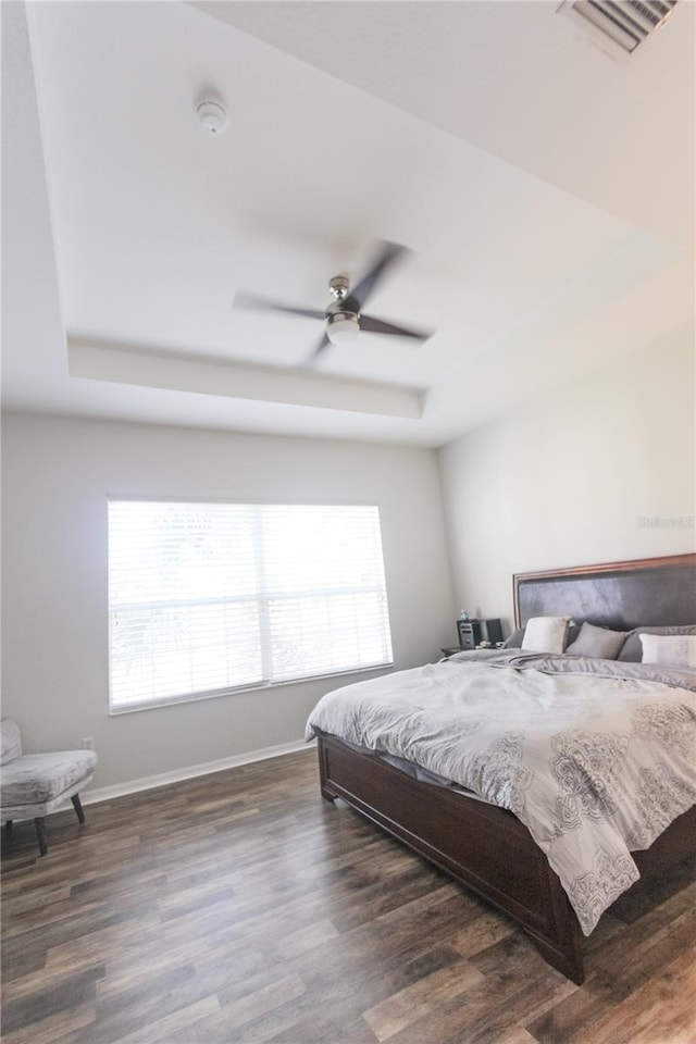 bedroom with a raised ceiling, ceiling fan, and dark wood-type flooring