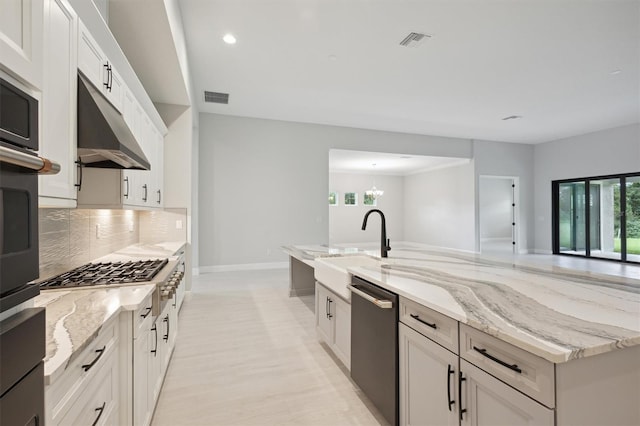 kitchen with appliances with stainless steel finishes, decorative backsplash, white cabinets, light stone countertops, and a notable chandelier