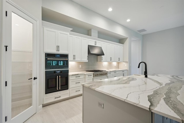 kitchen with double oven, white cabinetry, light stone counters, and tasteful backsplash