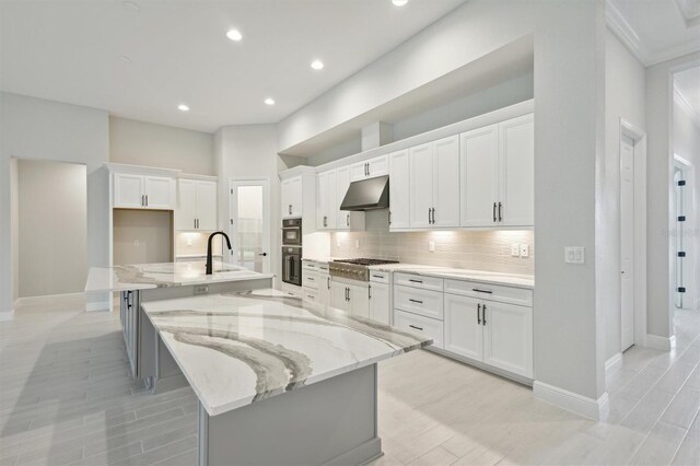 kitchen featuring stainless steel appliances, white cabinetry, light stone counters, and a large island with sink