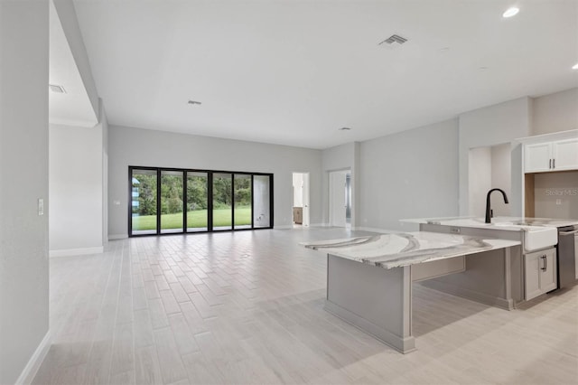 kitchen with light wood-type flooring, an island with sink, white cabinetry, light stone countertops, and stainless steel dishwasher