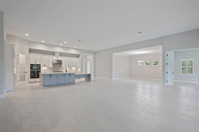 unfurnished living room featuring light hardwood / wood-style floors, sink, and a chandelier