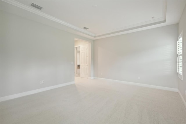 empty room featuring a tray ceiling, ornamental molding, and light carpet