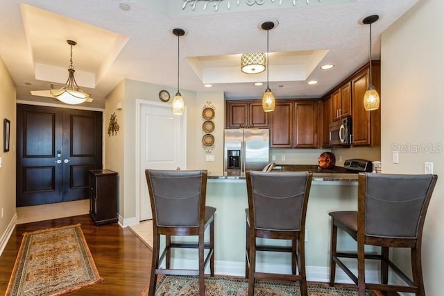 kitchen with stainless steel appliances, pendant lighting, dark hardwood / wood-style floors, a raised ceiling, and kitchen peninsula