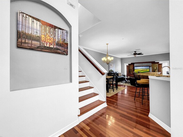 staircase with wood-type flooring, ceiling fan with notable chandelier, and crown molding