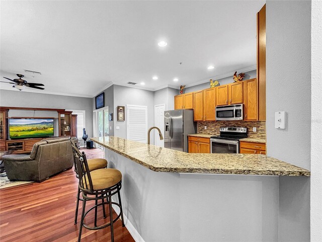 kitchen with kitchen peninsula, backsplash, light stone counters, a breakfast bar, and stainless steel appliances