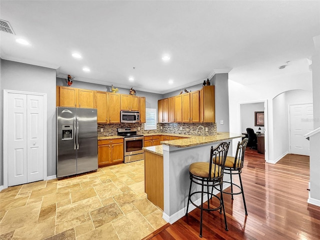 kitchen with light stone countertops, a kitchen breakfast bar, tasteful backsplash, kitchen peninsula, and appliances with stainless steel finishes