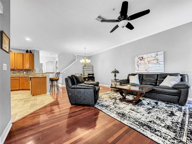 living room featuring light hardwood / wood-style flooring, ceiling fan with notable chandelier, and ornamental molding