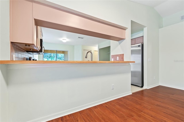 kitchen featuring high end fridge, sink, light wood-type flooring, and kitchen peninsula