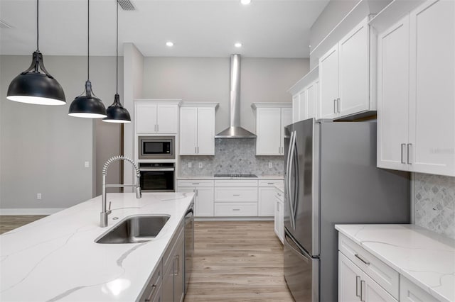 kitchen with light stone countertops, white cabinetry, sink, stainless steel appliances, and wall chimney range hood