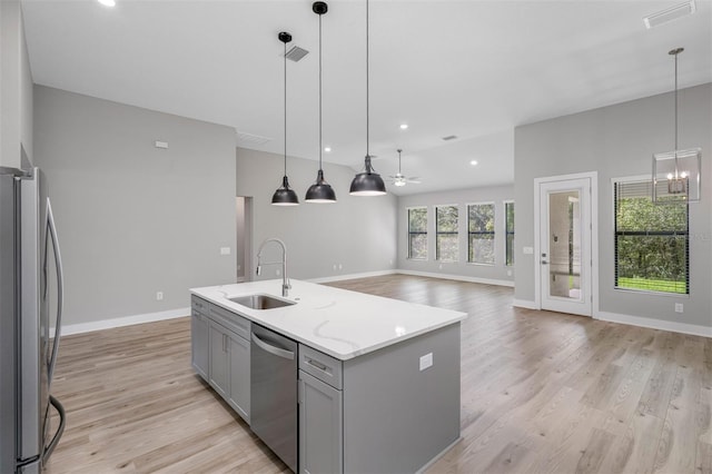 kitchen featuring light stone countertops, stainless steel appliances, gray cabinets, a center island with sink, and ceiling fan with notable chandelier