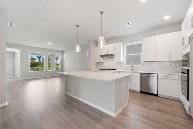 kitchen featuring light wood-type flooring, stainless steel appliances, a kitchen island, decorative light fixtures, and white cabinetry