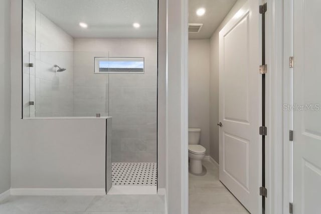 bathroom with a tile shower, tile patterned flooring, and toilet