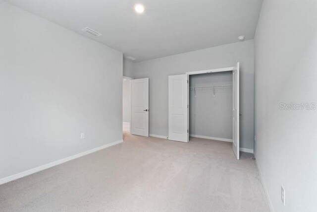 unfurnished bedroom with light colored carpet and a closet