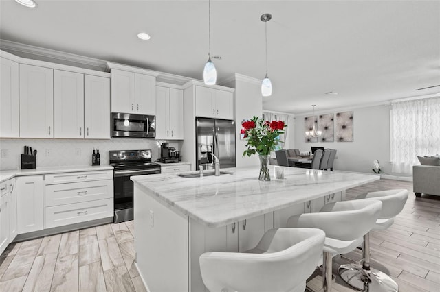 kitchen with a center island with sink, pendant lighting, crown molding, stainless steel appliances, and white cabinets