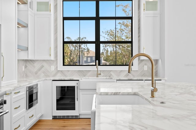 kitchen with white cabinetry, light stone countertops, stainless steel microwave, and beverage cooler