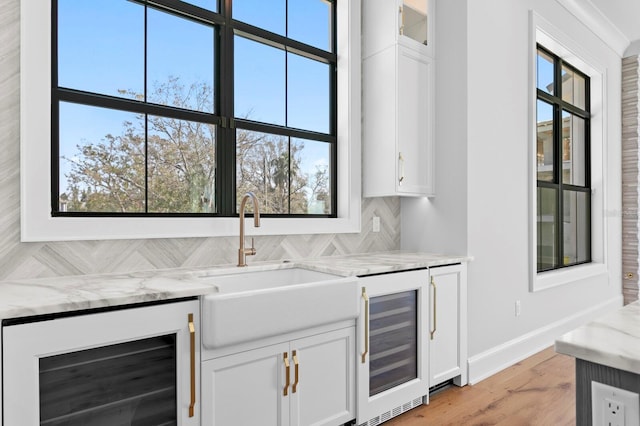 bar featuring light stone countertops, beverage cooler, and white cabinets