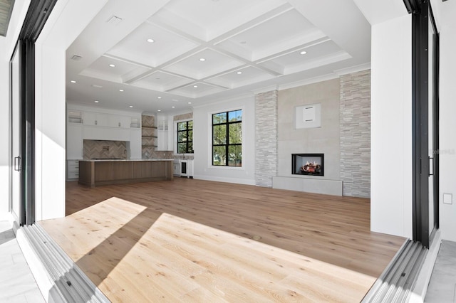 unfurnished living room featuring coffered ceiling, crown molding, light hardwood / wood-style flooring, a tile fireplace, and beam ceiling