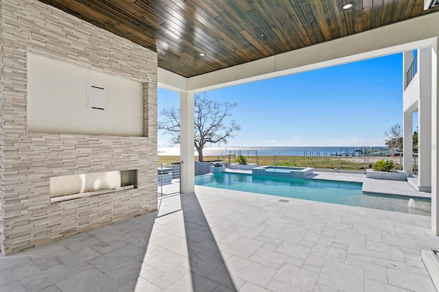 view of swimming pool with a patio, a water view, and an in ground hot tub