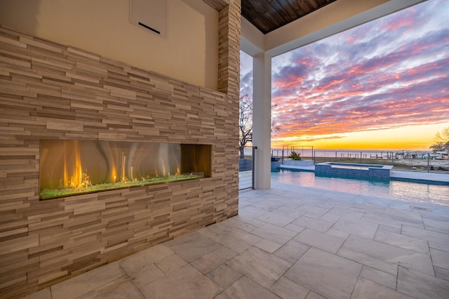 patio terrace at dusk featuring an in ground hot tub and a fireplace