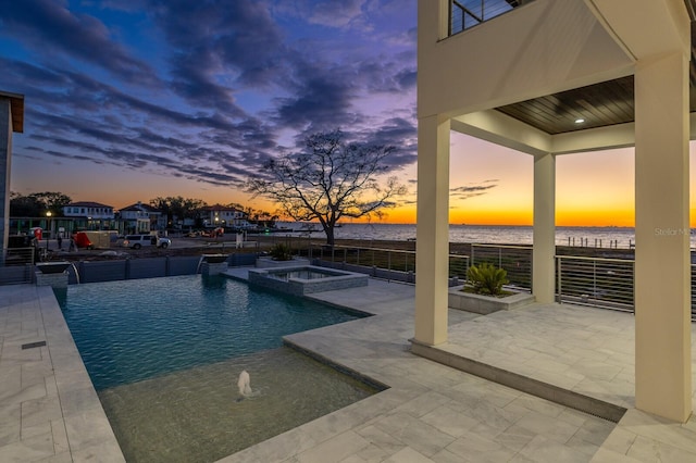 pool at dusk featuring a water view, pool water feature, an in ground hot tub, and a patio