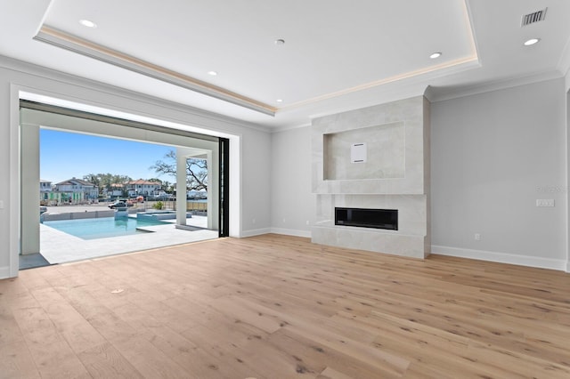 unfurnished living room featuring ornamental molding, a fireplace, light hardwood / wood-style floors, and a raised ceiling