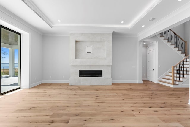 unfurnished living room with a raised ceiling, ornamental molding, light wood-type flooring, and a fireplace