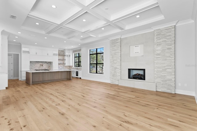 unfurnished living room with a multi sided fireplace, ornamental molding, coffered ceiling, and light wood-type flooring