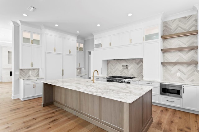 kitchen with white cabinetry, stainless steel microwave, a kitchen island with sink, and stove