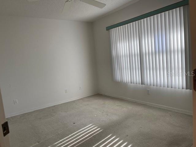 carpeted empty room featuring a ceiling fan, a textured ceiling, and baseboards
