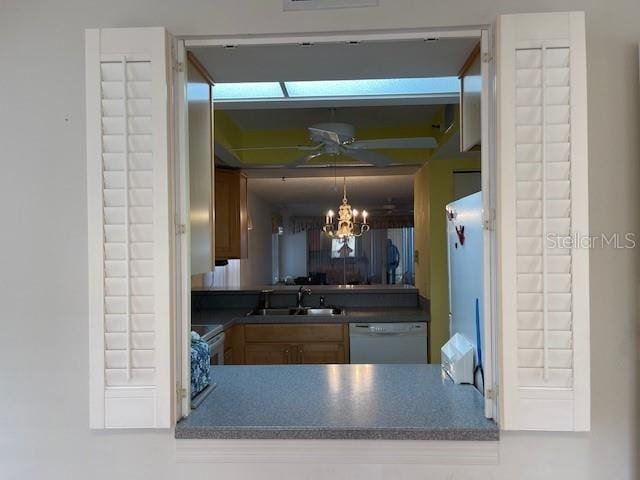 kitchen with dark countertops, dishwasher, ceiling fan with notable chandelier, and a sink