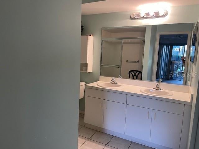 bathroom featuring tile patterned floors, a shower stall, double vanity, and a sink