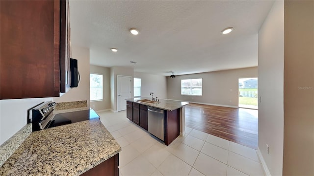 kitchen featuring light stone counters, dark brown cabinetry, stainless steel appliances, sink, and an island with sink