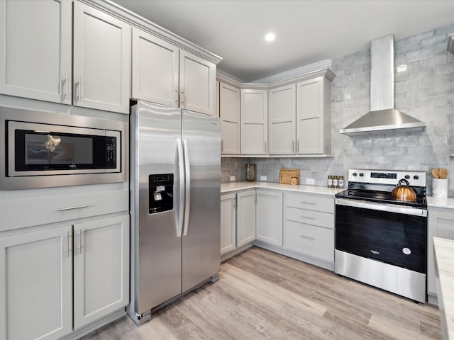 kitchen with decorative backsplash, appliances with stainless steel finishes, light wood-type flooring, and wall chimney exhaust hood