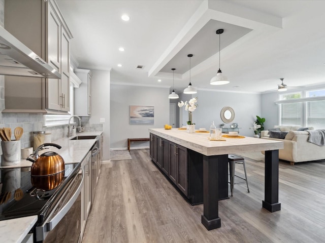 kitchen with wall chimney exhaust hood, stainless steel electric stove, ceiling fan, pendant lighting, and a kitchen island