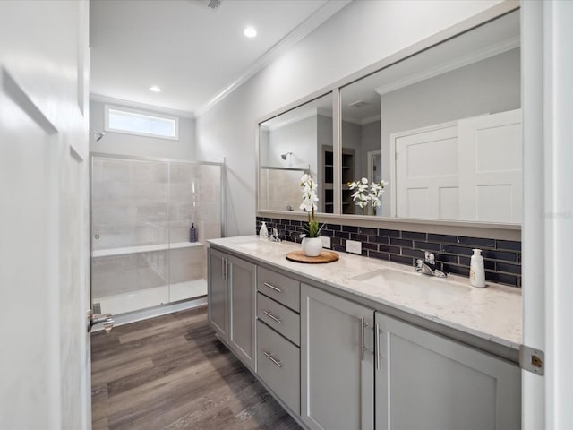 bathroom featuring vanity, a shower with shower door, backsplash, crown molding, and wood-type flooring