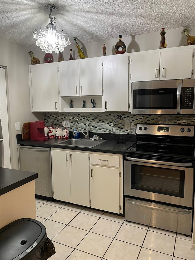 kitchen featuring light tile patterned floors, a chandelier, appliances with stainless steel finishes, decorative backsplash, and sink