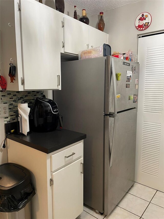 kitchen featuring white cabinets, stainless steel refrigerator, a textured ceiling, light tile patterned floors, and backsplash