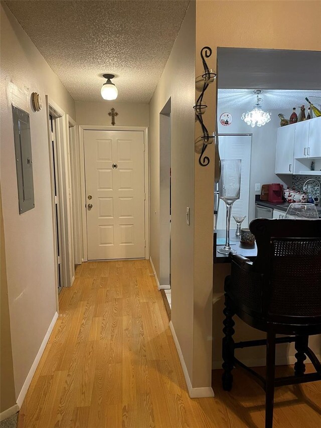 corridor with a textured ceiling, sink, light hardwood / wood-style flooring, and electric panel