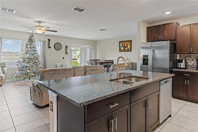 kitchen with appliances with stainless steel finishes, dark brown cabinets, ceiling fan, sink, and an island with sink