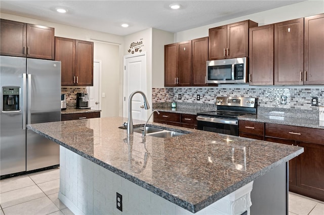 kitchen featuring sink, stainless steel appliances, an island with sink, dark stone counters, and light tile patterned flooring