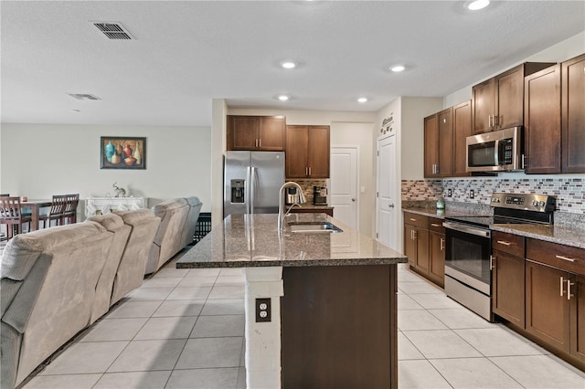 kitchen featuring decorative backsplash, appliances with stainless steel finishes, sink, an island with sink, and light tile patterned flooring