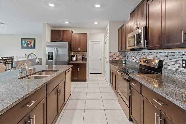 kitchen featuring sink, decorative backsplash, dark stone countertops, light tile patterned floors, and stainless steel appliances