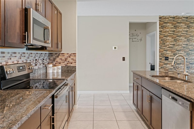 kitchen with sink, backsplash, dark stone counters, light tile patterned floors, and appliances with stainless steel finishes