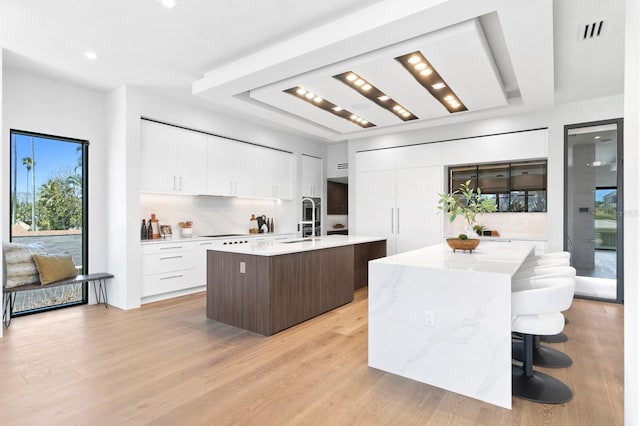 kitchen with a breakfast bar, a kitchen island with sink, white cabinets, decorative backsplash, and light wood-type flooring