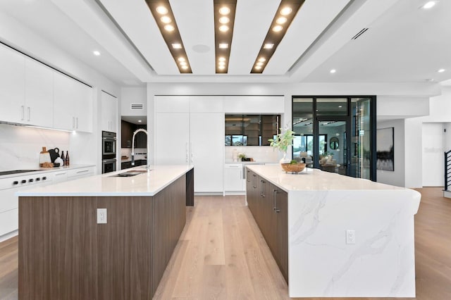 kitchen with backsplash, sink, a spacious island, and light wood-type flooring