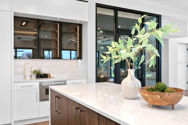 bar with tasteful backsplash, light stone counters, dark brown cabinetry, white cabinets, and oven