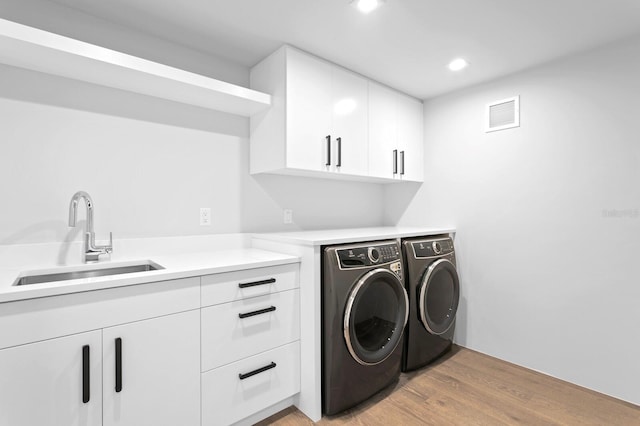 laundry area with cabinets, independent washer and dryer, sink, and light hardwood / wood-style flooring