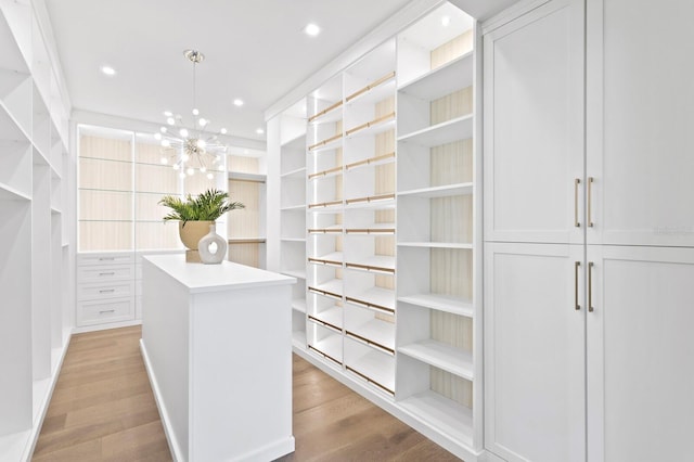 spacious closet with light hardwood / wood-style floors and a notable chandelier