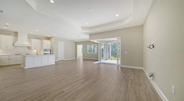 unfurnished living room featuring sink, a raised ceiling, and light wood-type flooring